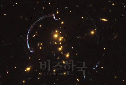 암흑물질을 잔뜩 머금은 무거운 은하단은 육중한 질량으로 주변의 시공간을 심하게 왜곡한다. 은하단보다 더 먼 배경의 은하들의 빛이 은하단이 왜곡한 시공간을 지나면서 빛의 경로가 휘어져 은하단 주변에 일그러진 허상을 만들어낸다. 마치 중력이 렌즈처럼 빛의 경로를 휘게 한다고 해서 이 현상을 중력 렌즈(Gravitational lensing)라고 부른다. 중력으로 만들어지는 우주 신기루인 셈이다. 사진=NASA, ESA, H. Lee & H. Ford (Johns Hopkins U.)